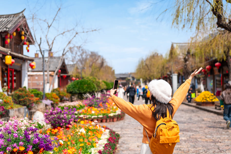 ciudad de lijiang con hermosas flores y una chica de amarillo con mochila amarilla